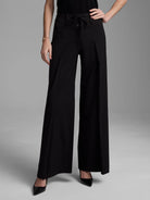 Black high-waisted wide-leg pants feature an apron-style front, drawstring, and single button closure.