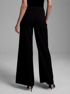 Black high-waisted, wide-leg, floor-length pants, seen from behind, with subtle back welt pockets.