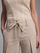 Light beige pants with a front self-tie waist, two gold buttons, and side pockets.
