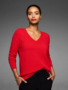 Red V-neck sweater on a model. Features ribbed trim at neck & cuffs, fine knit texture, and raglan sleeves.