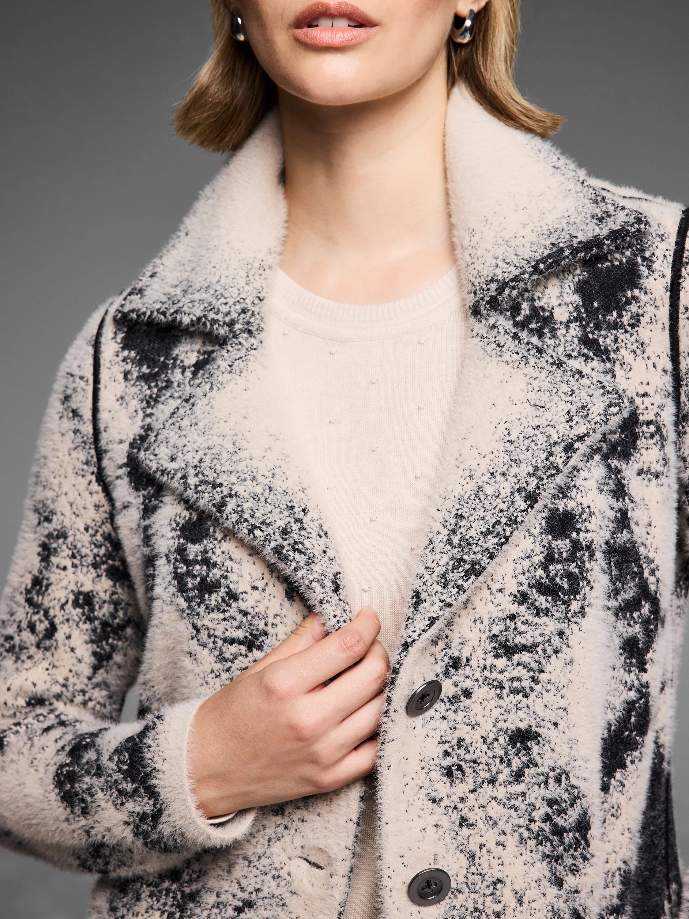 Cream & black textured knit coat with fuzzy speckled pattern, lapel collar, & visible dark buttons.