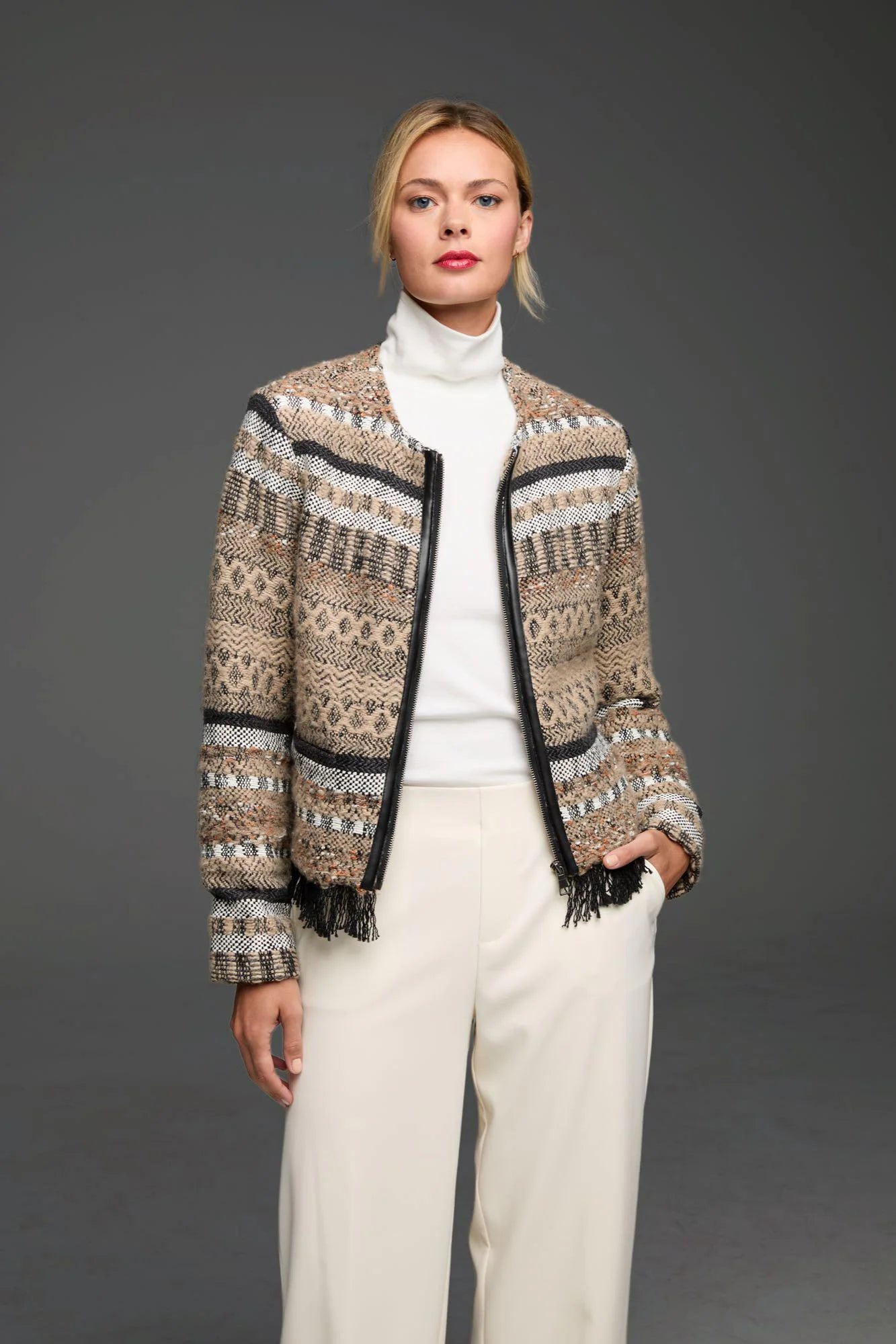 Beige, black, & white patterned knit jacket with geometric designs. Features smooth black trim & fringe along the open front.