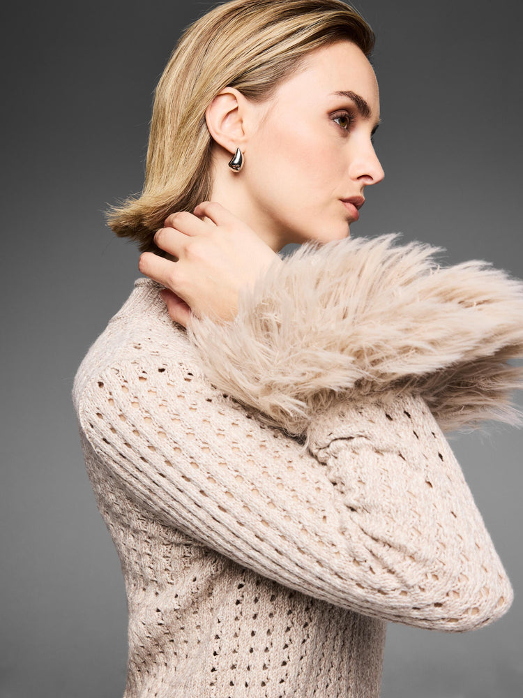 Pale beige fitted pointelle knit top features dramatic fluffy fur cuffs, styled on a model in profile.