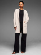 Cream long open knit coat with ribbed sleeves and two large front patch pockets.