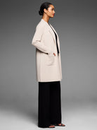 Cream open-front knit coat, knee-length, with ribbed long sleeves and two front patch pockets.