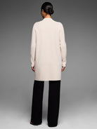 Cream knee-length coat shown from back. Features a collarless design and long ribbed sleeves.