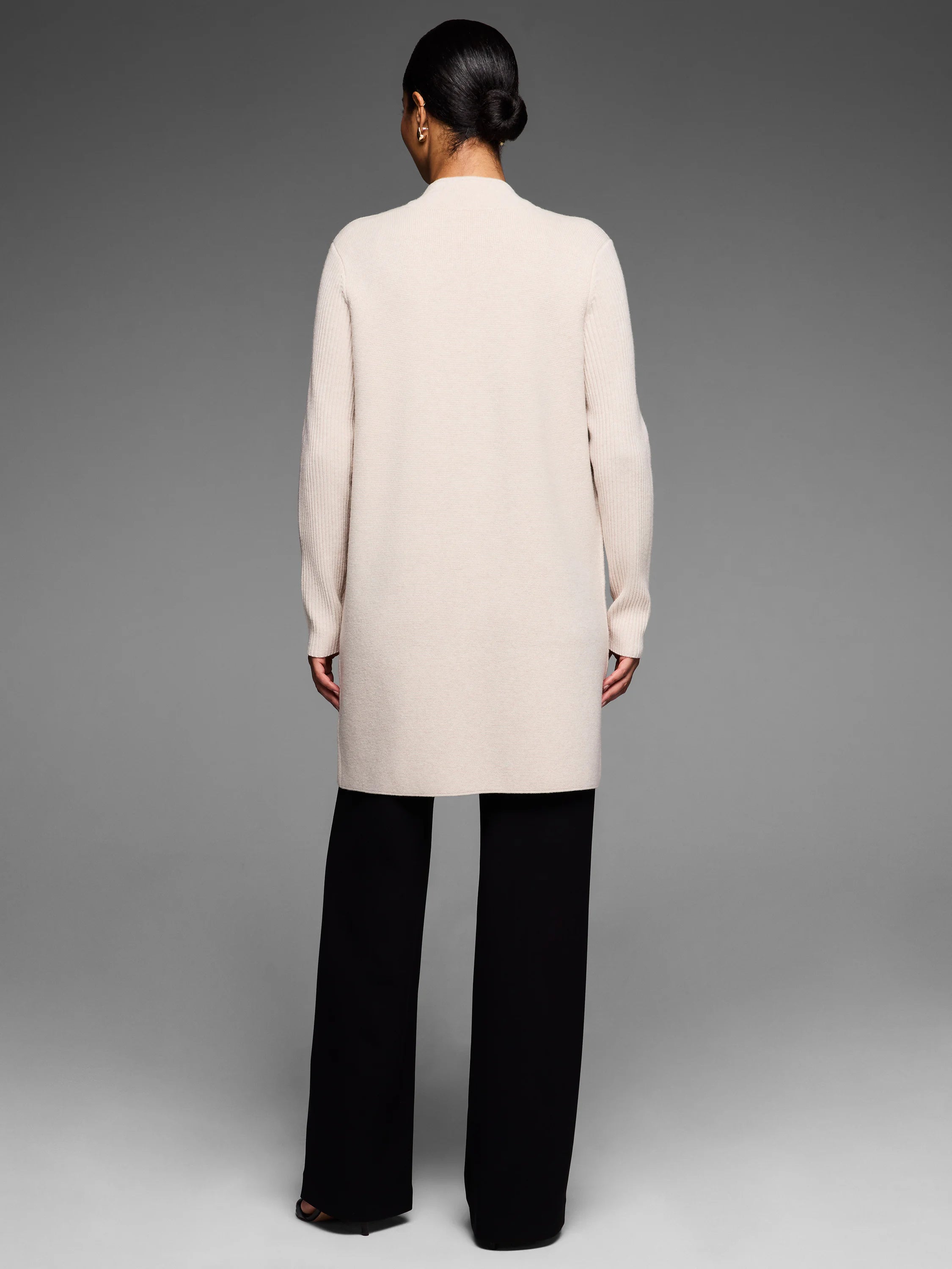 Cream knee-length coat shown from back. Features a collarless design and long ribbed sleeves.