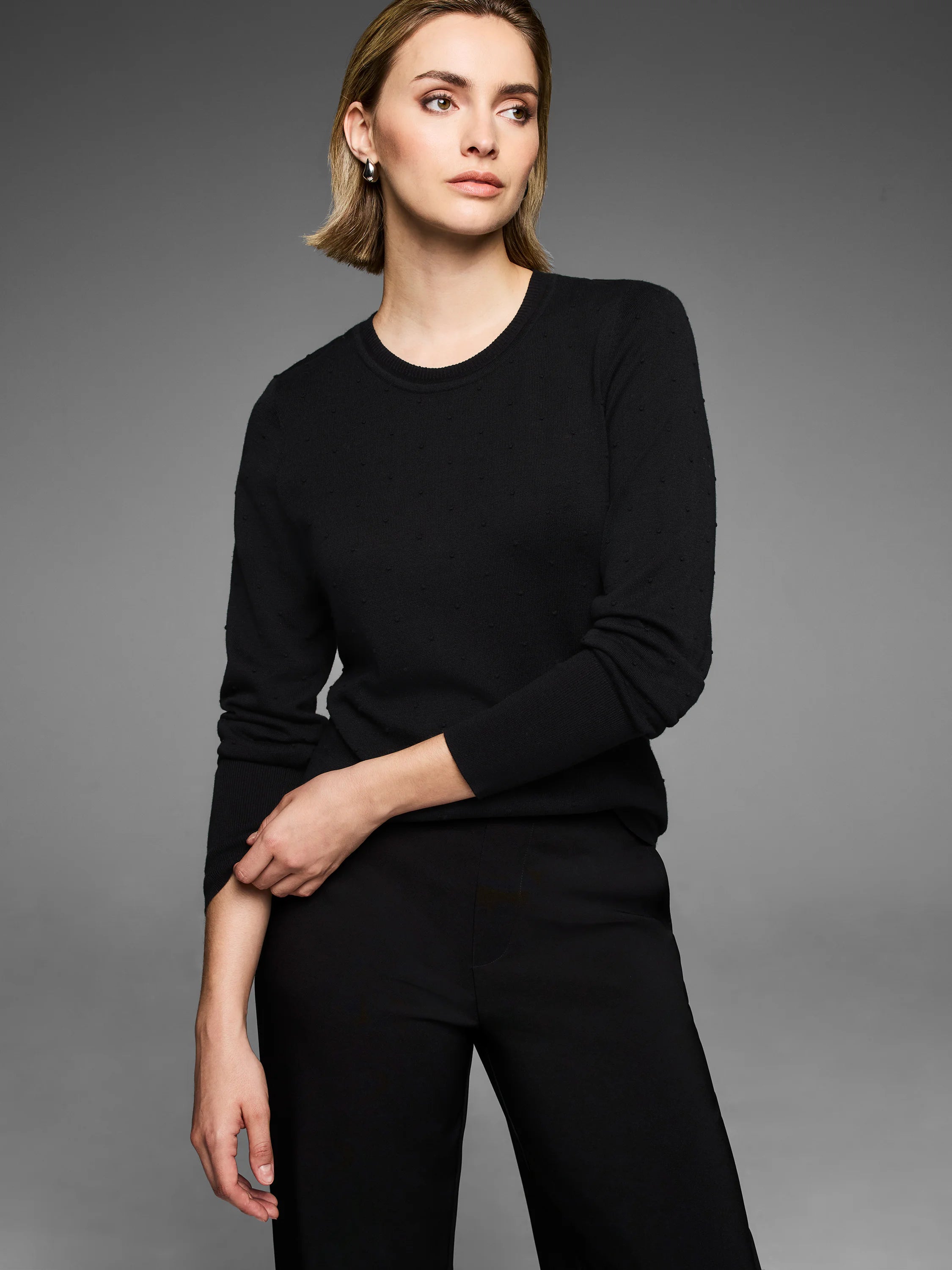 Black round-neck sweater with a subtle dotty texture, long sleeves.