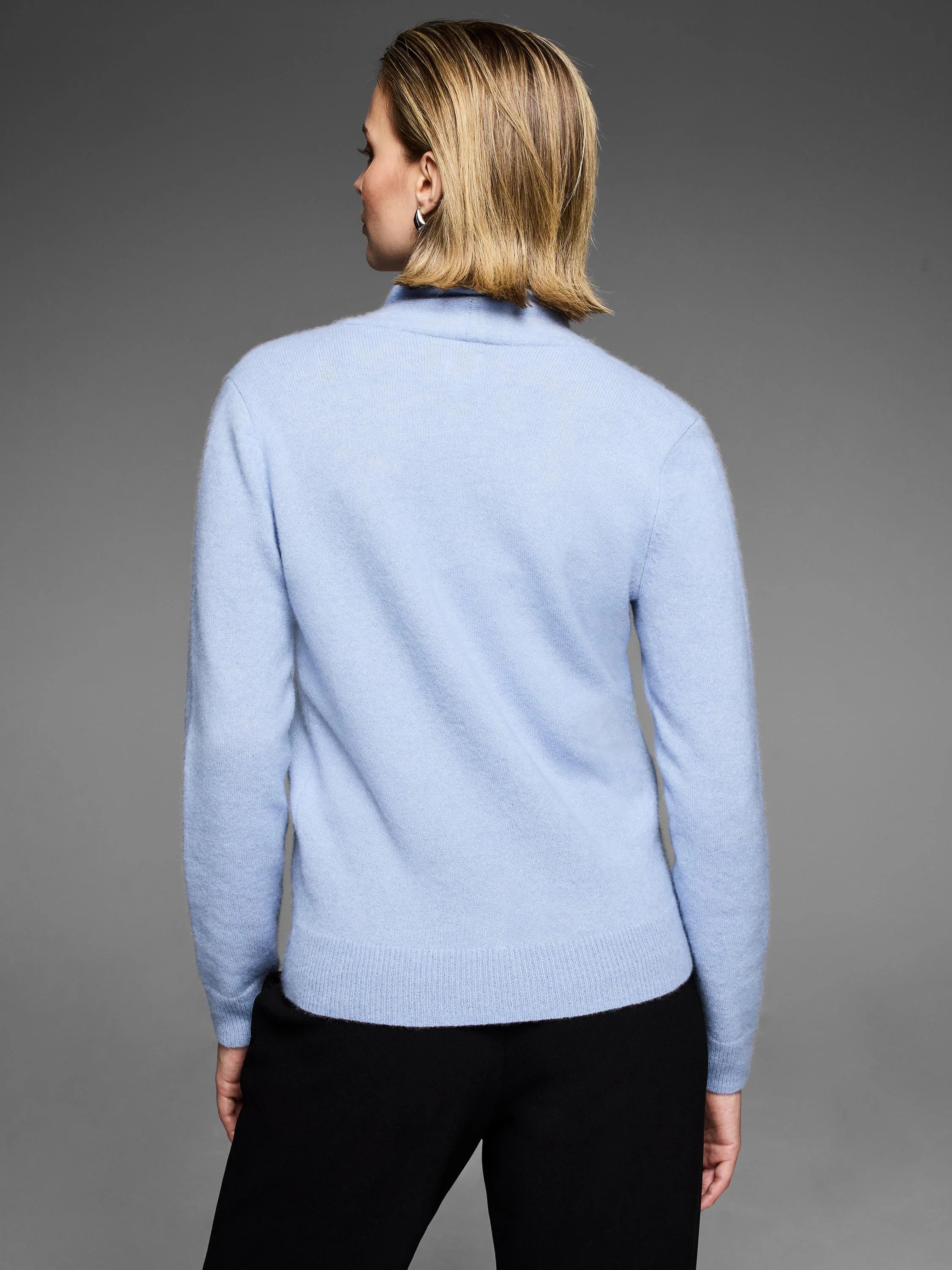 Light blue cashmere sweater shown from the back on a woman. Features a built-up neck, long sleeves, and ribbed hem/cuffs.