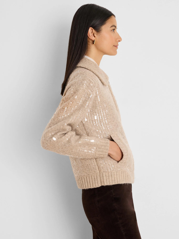 Tan knit jacket with a collar, ribbed cuffs, and shimmering sequins. Model's hand in pocket.