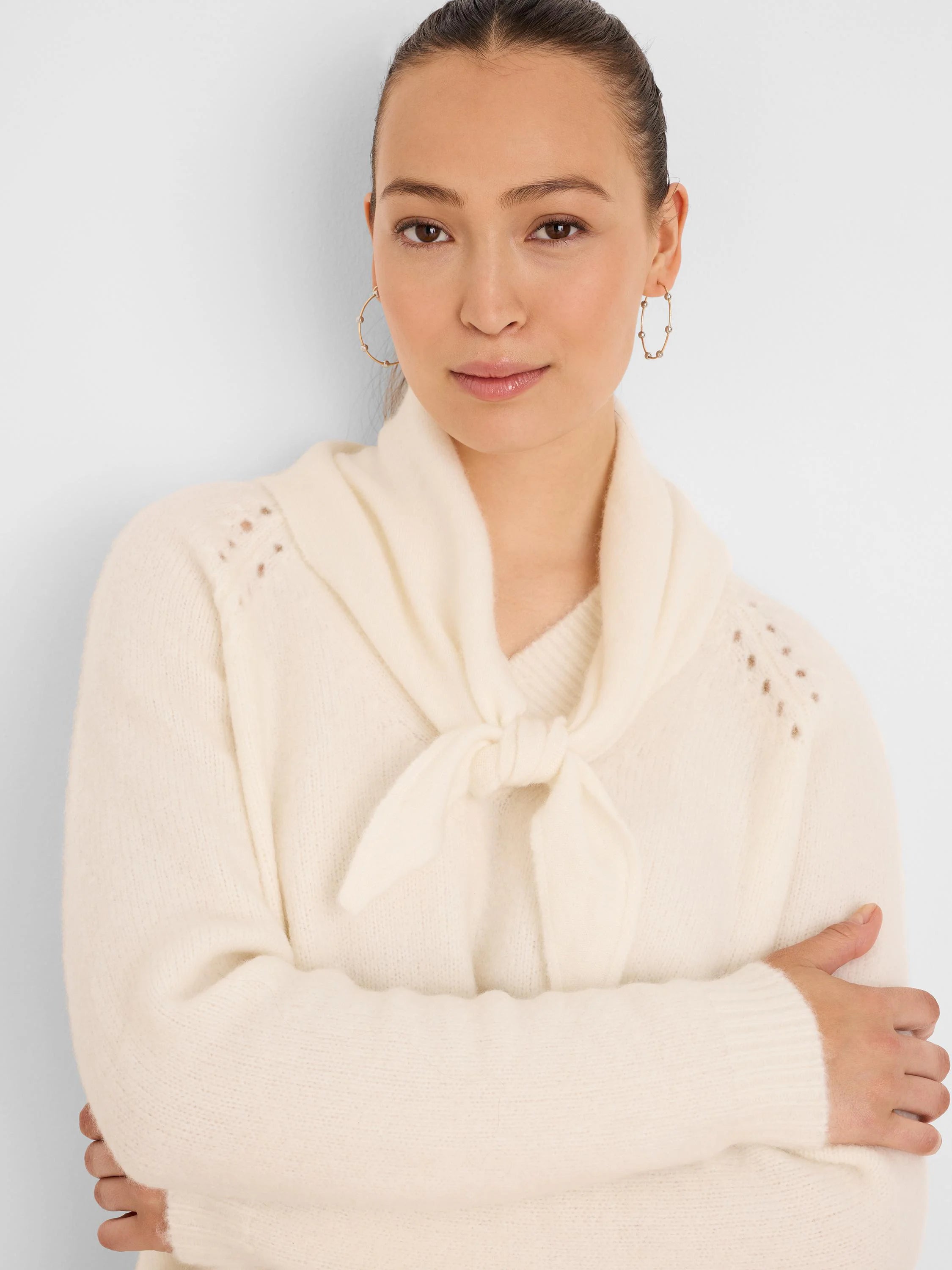 Cream V-neck sweater featuring a tied scarf neck and decorative openwork details on the shoulders.