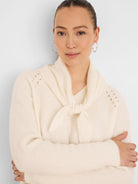 Cream V-neck sweater featuring a tied scarf neck and decorative openwork details on the shoulders.