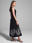 Black sleeveless midi dress with white embroidered leaf details at the hem.
