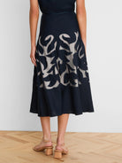 Dark blue A-line midi skirt with cut-out leaf patterns revealing light beige fabric underneath.
