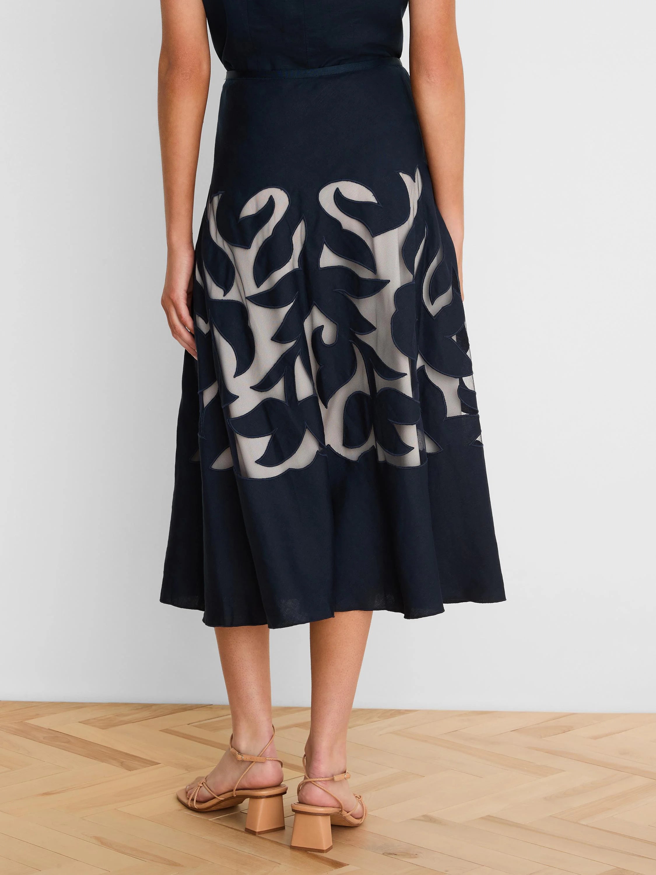 Dark blue A-line midi skirt with cut-out leaf patterns revealing light beige fabric underneath.