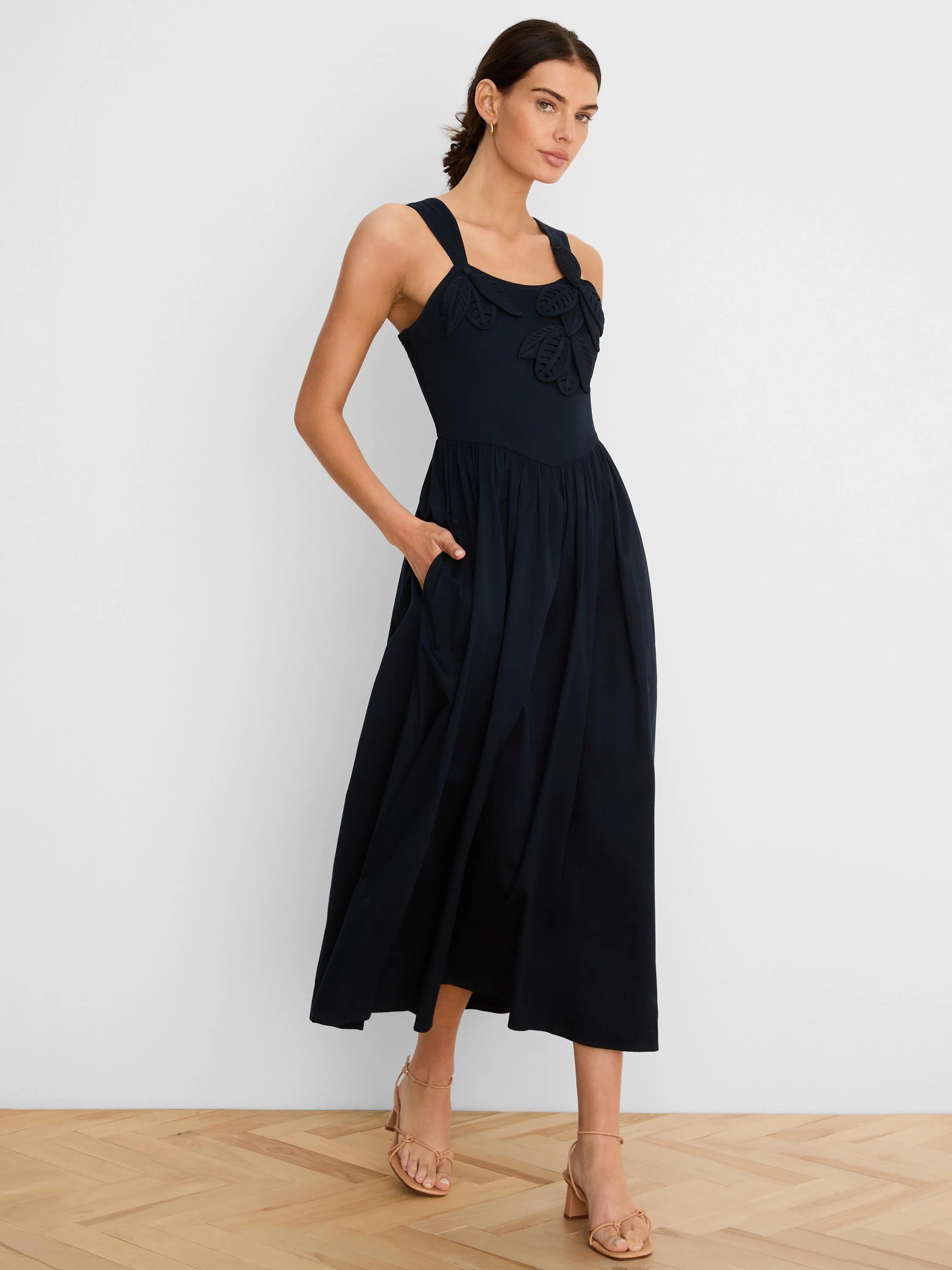 Navy midi dress with leaf appliques on bodice, sleeveless, v-waist, full skirt, and side pockets.