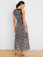 Dark maxi dress with creamy floral burnout pattern, sleeveless, high neck, and tied waist, viewed from the back.
