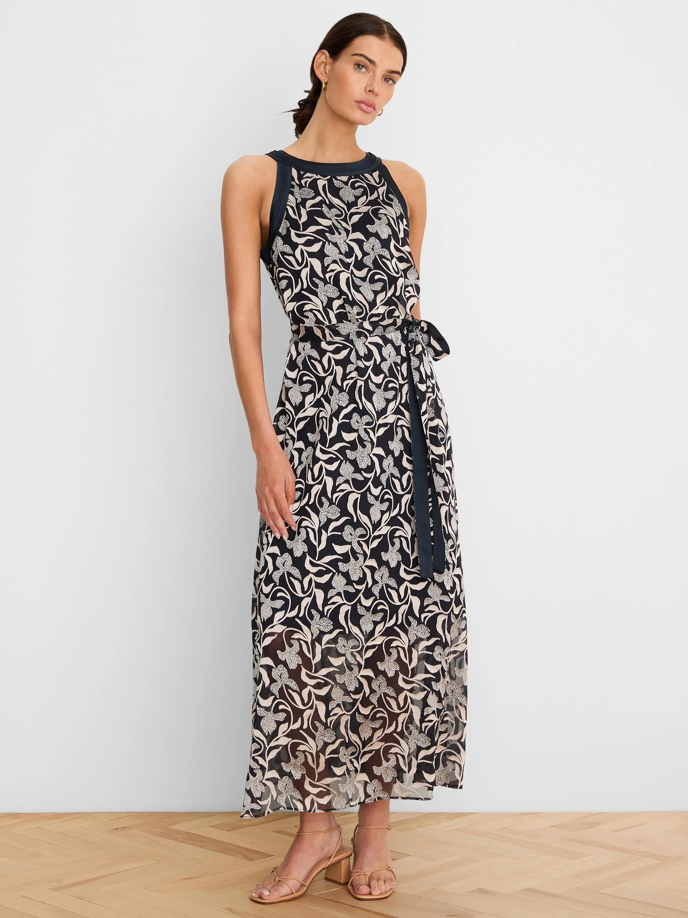 Dark maxi dress with beige floral burnout pattern, sleeveless, round neck, and a tie waist belt.