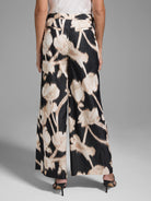 Black wide-leg pants with a beige floral print.  The flowers are abstract and slightly blurred.