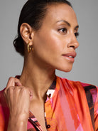 Shirtdress with orange, pink, and brown abstract print. Glossy fabric.  Dark hair and gold hoop earrings visible.