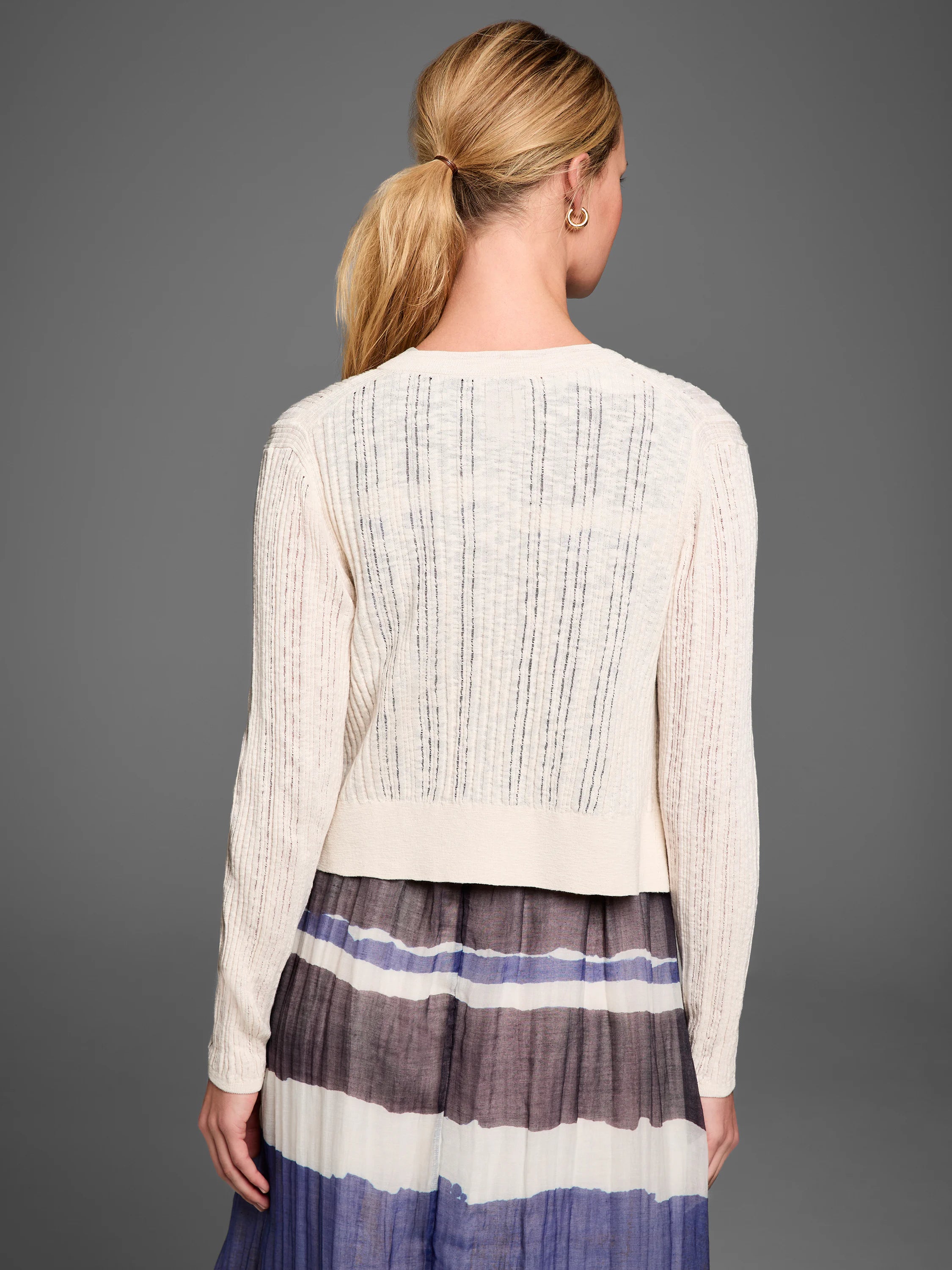 Back view of a cream pointelle stitch cardigan with vertical open-knit patterns, long sleeves, and ribbed trim.