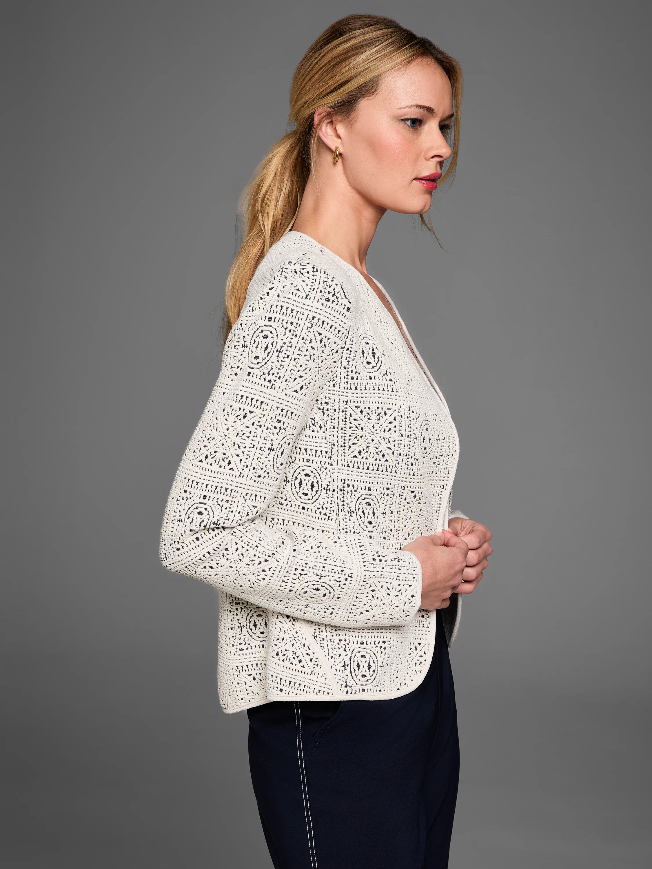 Cream tapestry knit jacket with open geometric patterns, worn open, showing dark contrast underneath.