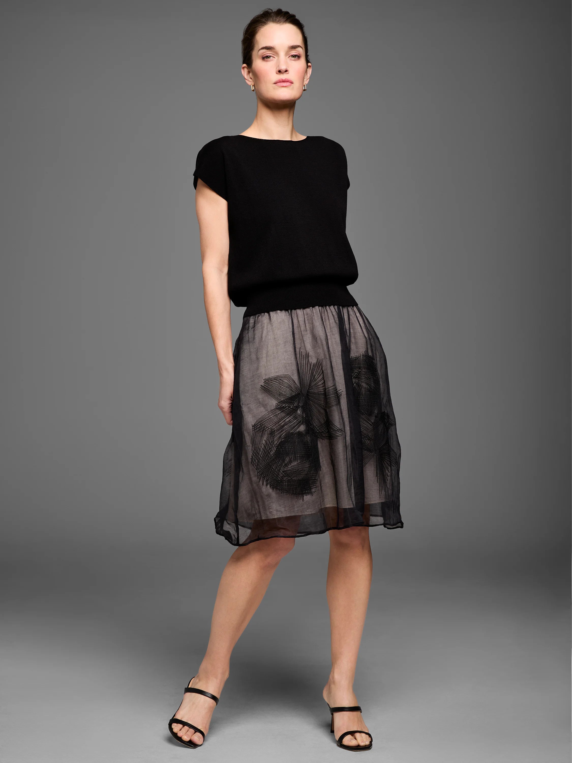 Black short-sleeved boat neck sweater with ribbed hem, paired with a sheer black embroidered skirt over a light lining.