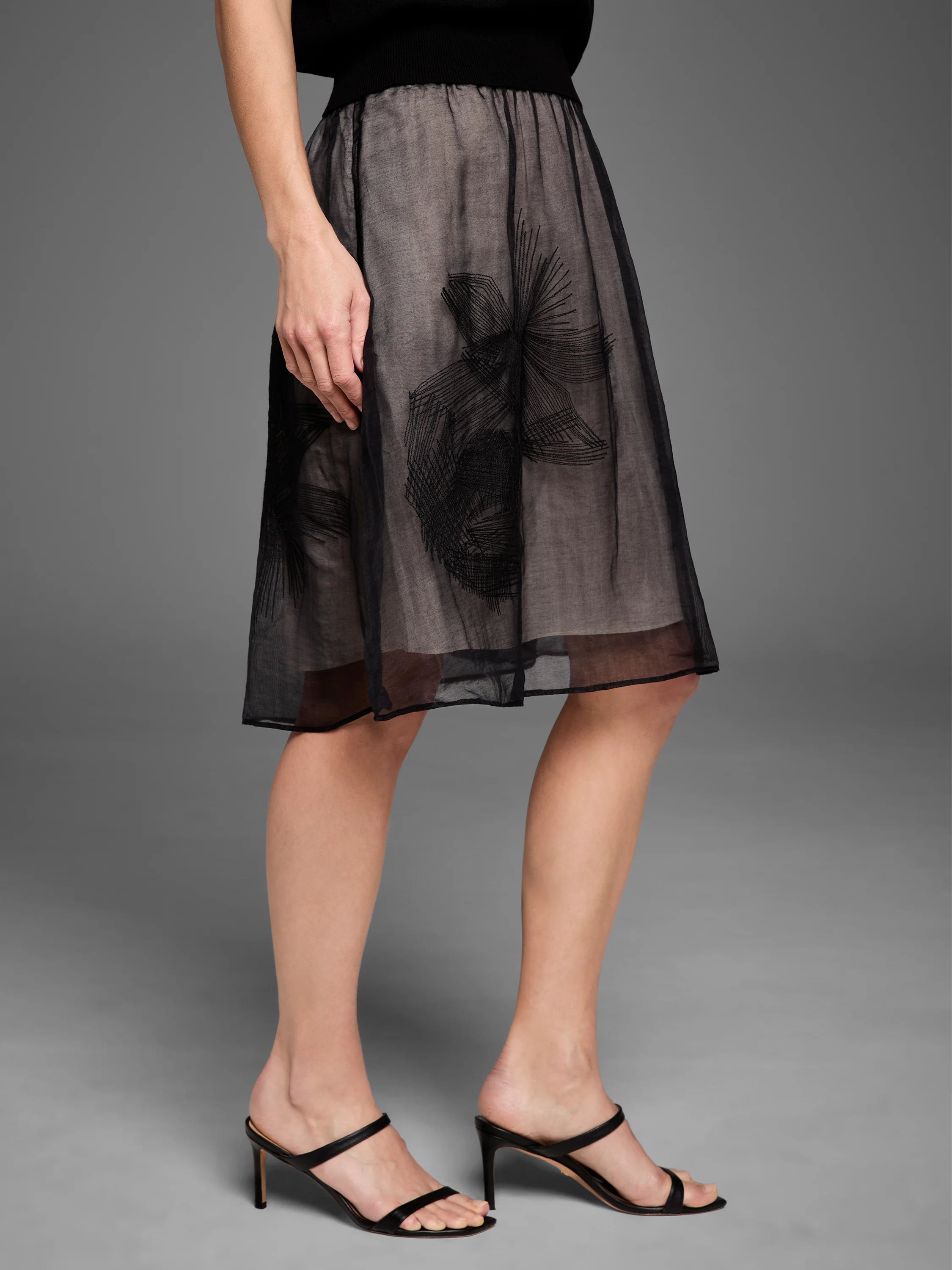 Black sheer mesh midi skirt with abstract black embroidery and a visible light lining, featuring a gathered waist.