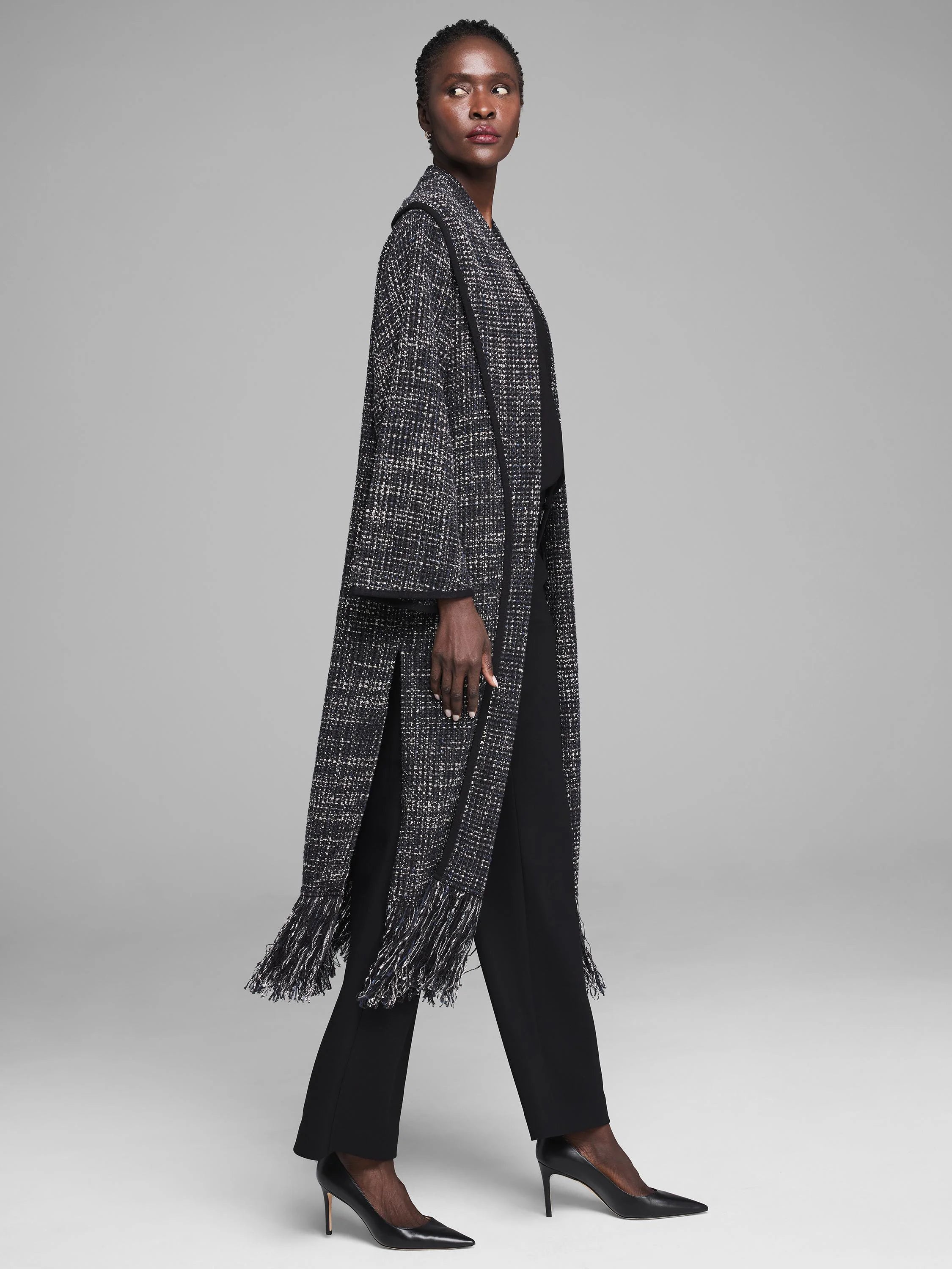 Long black and white tweed jacket with fringe hem and vertical slits.