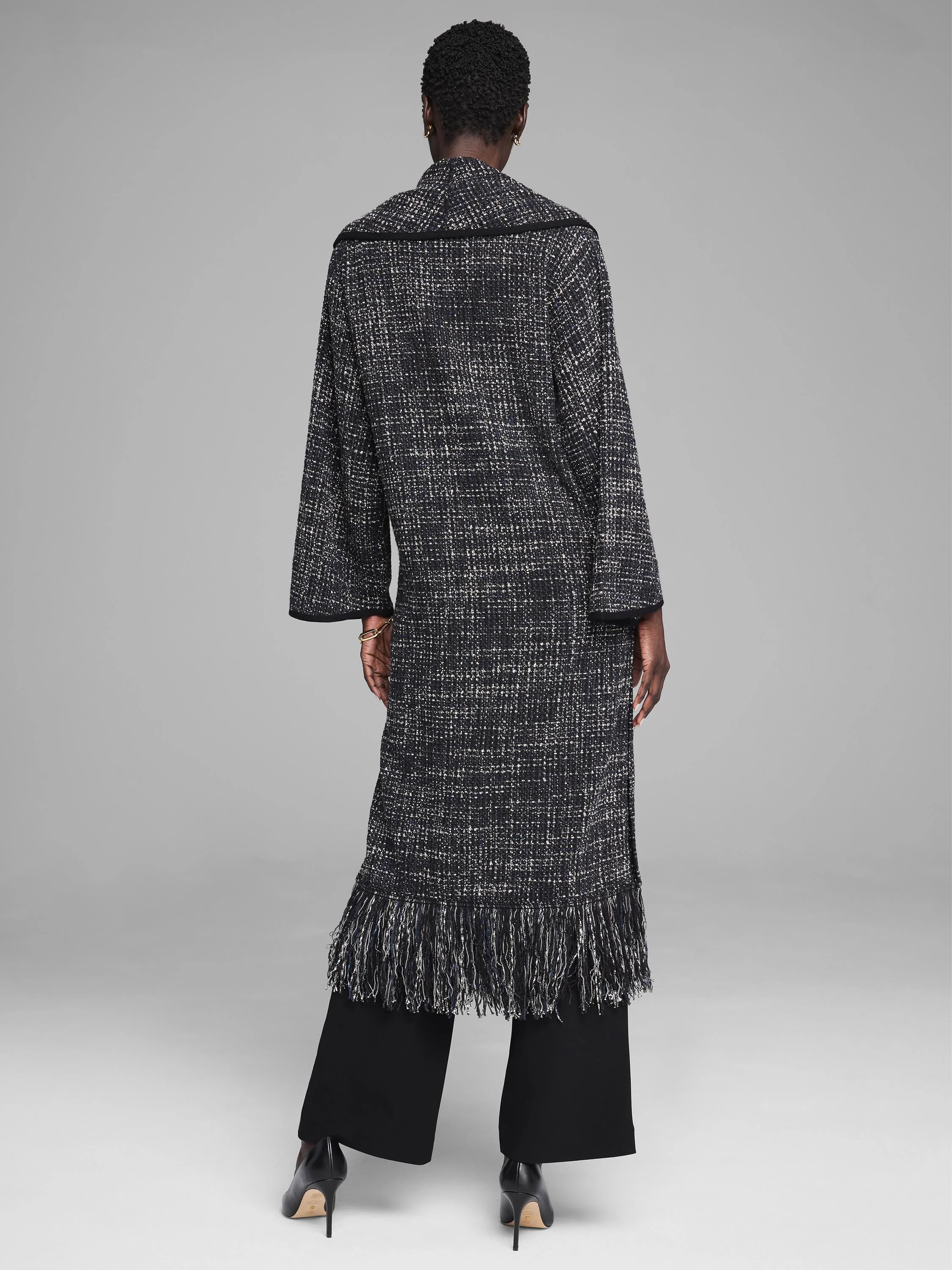 Long black & white tweed jacket with wide sleeves and a full fringe hem, shown from the back.
