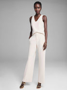 Cream wide-leg knit scuba trousers. High-waisted, with front pleats, side pockets, and a smooth, full-length drape.