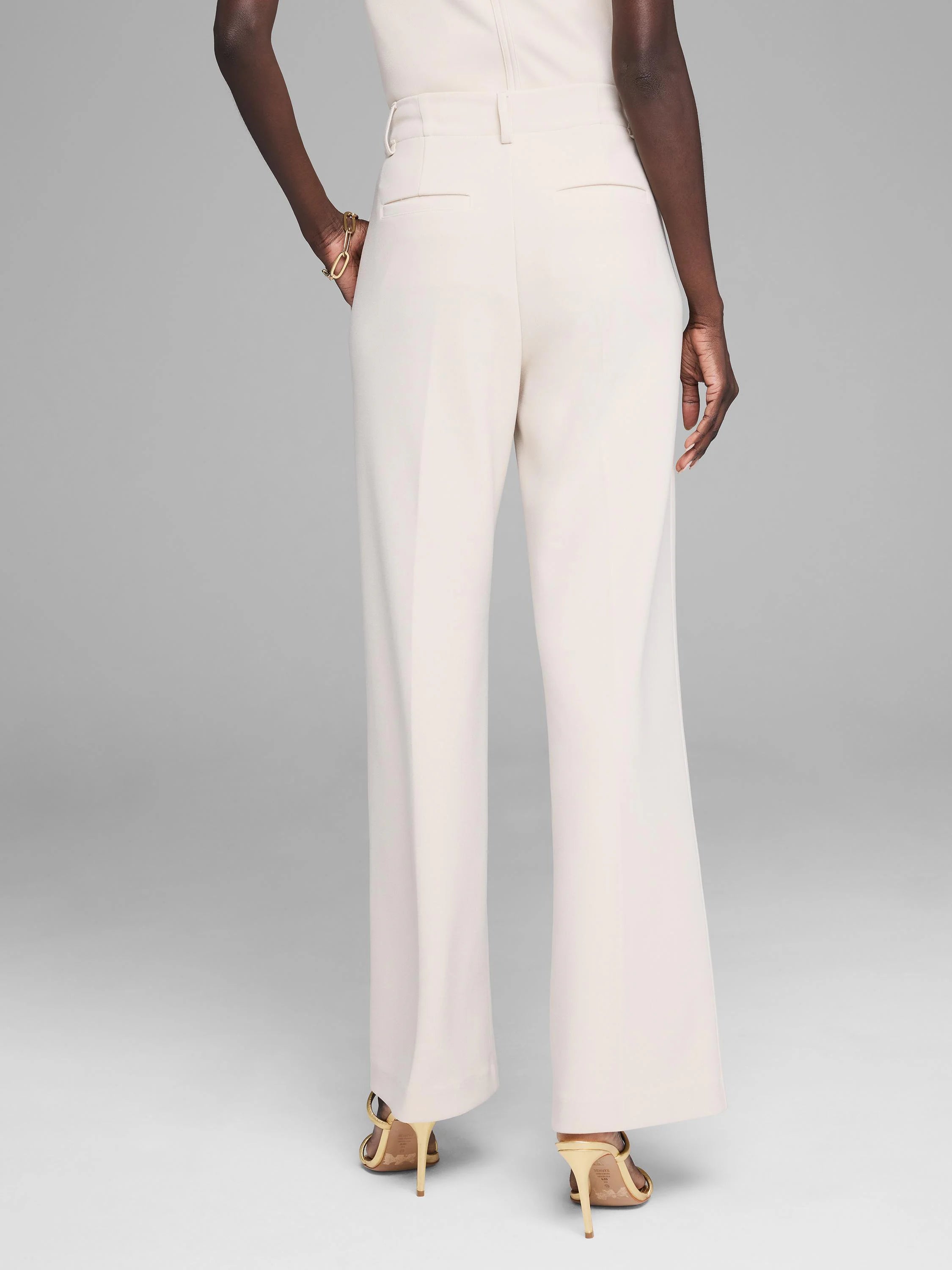 Light beige wide-leg trousers on a model, shown from the back. High-waisted, smooth fabric, with back pockets.