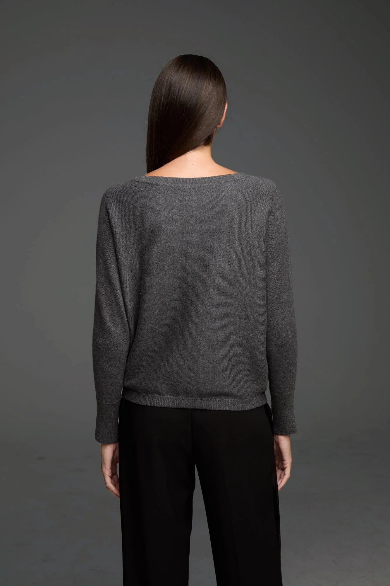 Dark grey knit sweater, viewed from the back on a model. Features a wide neckline, relaxed fit, and ribbed cuffs and hem.