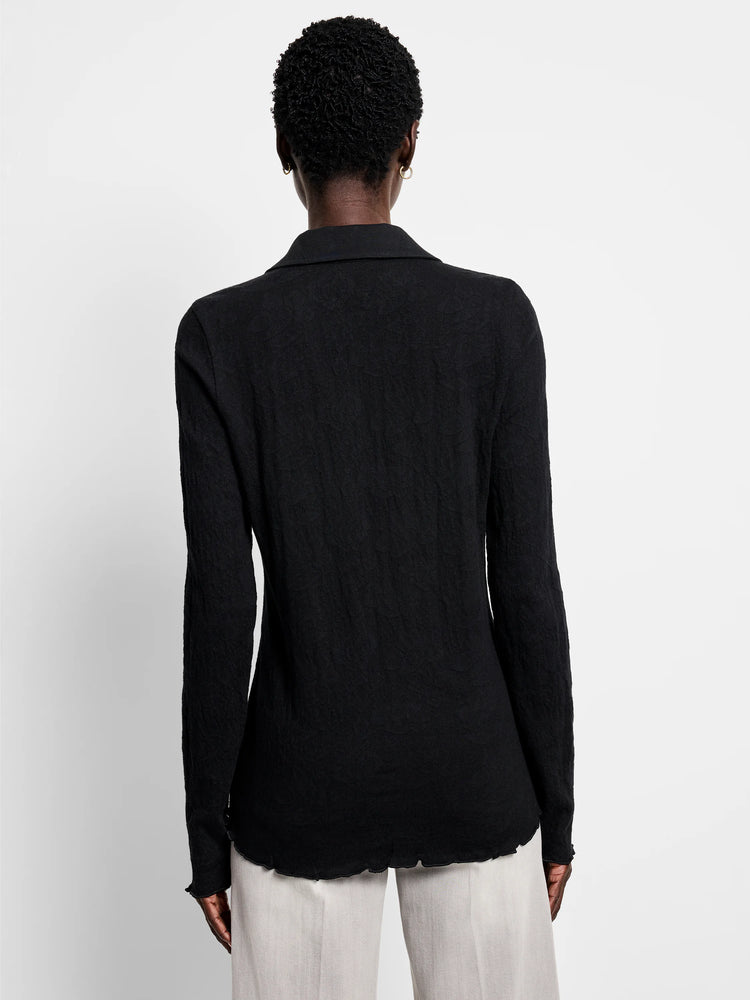 Back of black collared lace-knit top. Long sleeves, wavy lettuce-edge cuffs and hem.