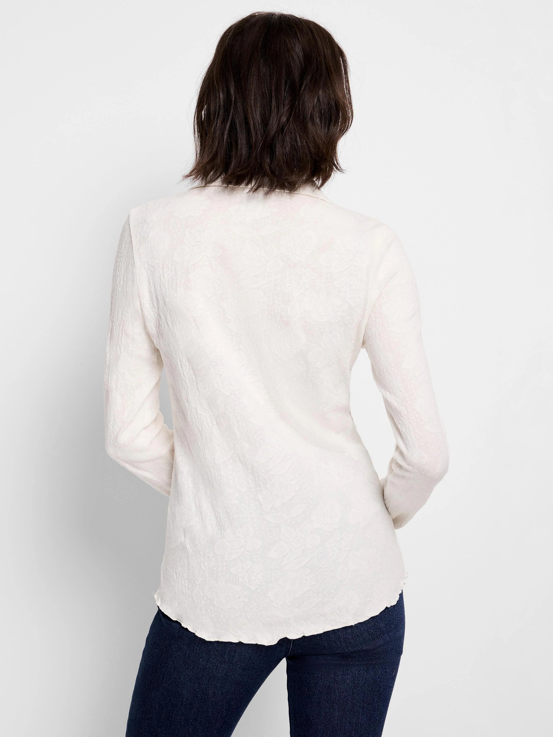 Off-white collared lace knit top, seen from back. Features subtle floral pattern, long sleeves, & scalloped hem.