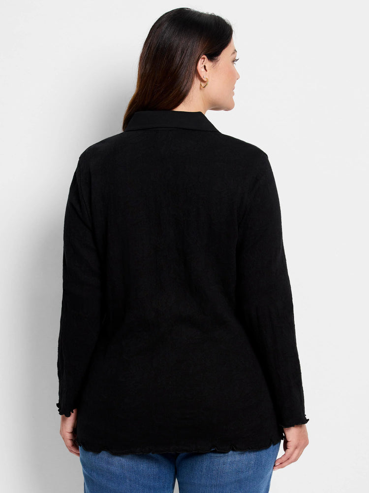 Black collared top, back view. Subtle lace knit pattern, long sleeves, and ruffled trim on cuffs and hem.