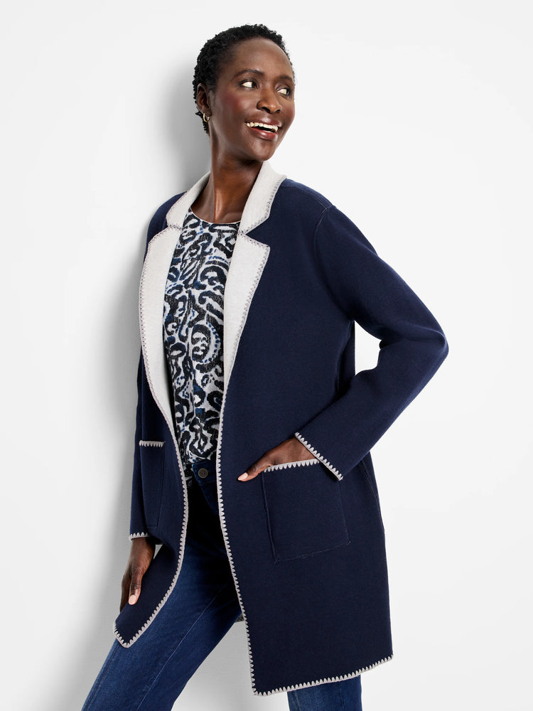 Navy knit jacket with light grey reversible lining visible on lapels, cuffs, pockets, and zig-zag stitched edges.