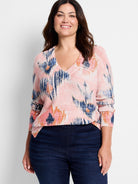 Light pink waffle knit V-neck sweater with bold, abstract brushstrokes in navy, light blue, orange, and white.