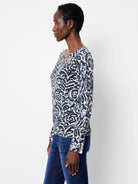 White sweater with black & blue abstract paisley print, crew neck, long sleeves with button cuffs.