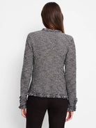 Black and white geometric knit jacket, seen from back. Features fringe along the neckline, hem, and cuffs.