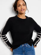 Black knit sweater with white loop-stitch trim along the shoulders and down the sleeves, forming decorative bands on the...