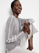 Grey knit sweater with white ladder stitching down the sleeves and ribbed cuffs.