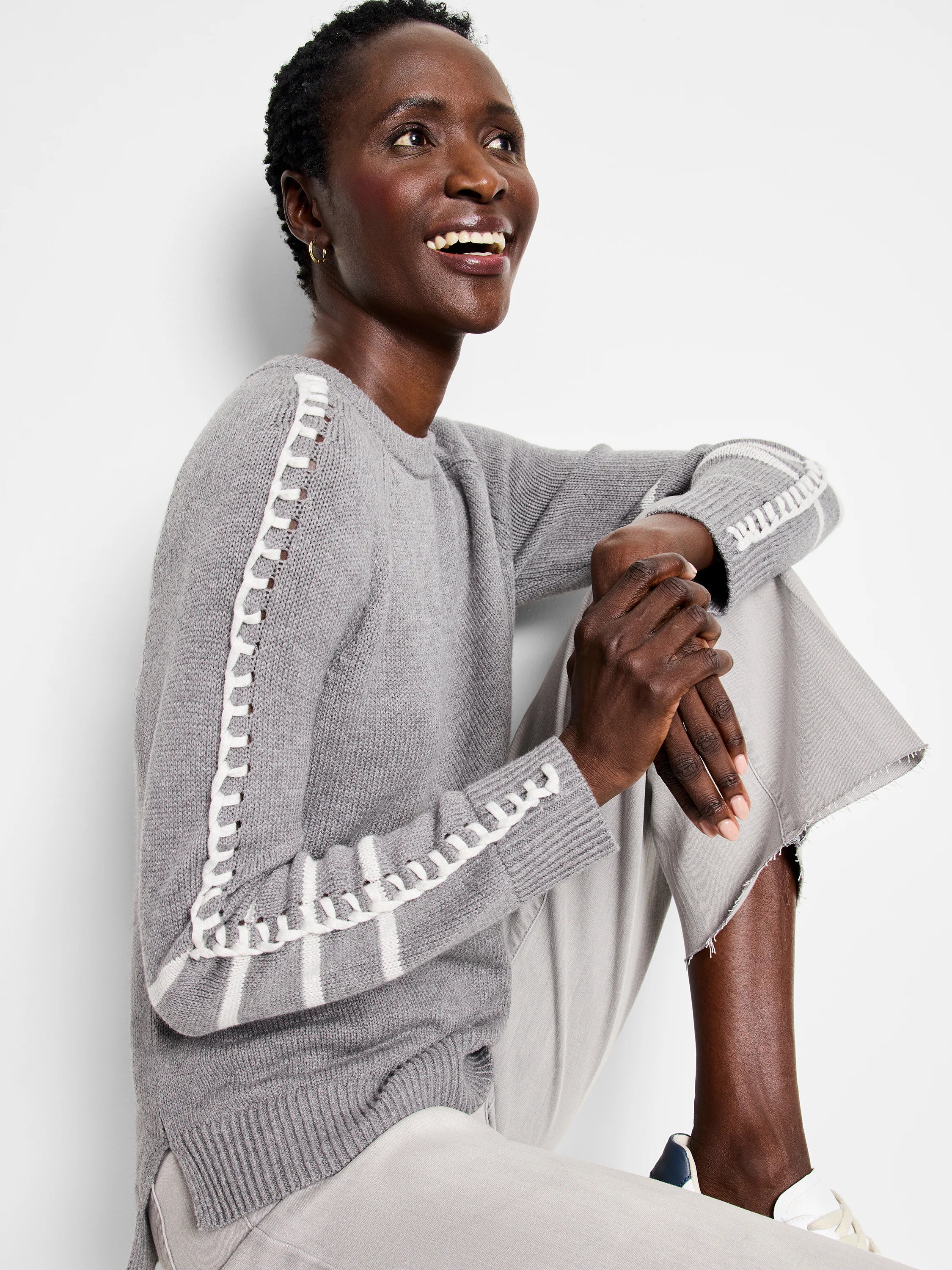 Grey knit sweater with white ladder stitching down the sleeves and ribbed cuffs.