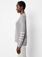 Light grey sweater with white braided trim down the sleeve seam and three white stripes on the upper arm.