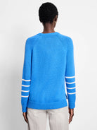 Blue knit sweater with three white horizontal stripes on each lower sleeve. Back view.