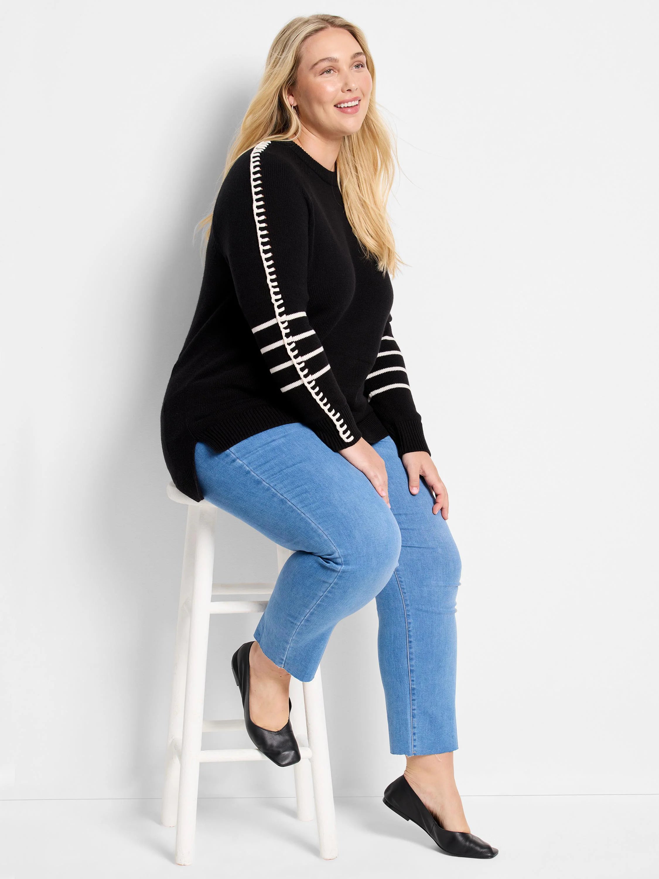 Black crewneck sweater with white vertical dash stitching on shoulders and horizontal white stripes on sleeves.