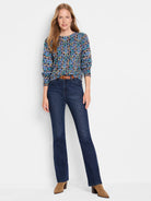 Woman in blue, green, brown patterned long-sleeve sweater; dark wash jeans; light brown boots.