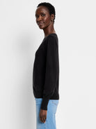 Black round-neck sweater with long, subtly voluminous sleeves gathered at ribbed cuffs and a ribbed hem, on a model.