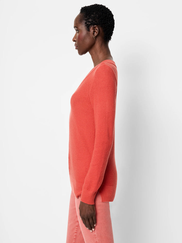 Coral waffle stitch V-neck sweater with long sleeves, worn by a model in profile.