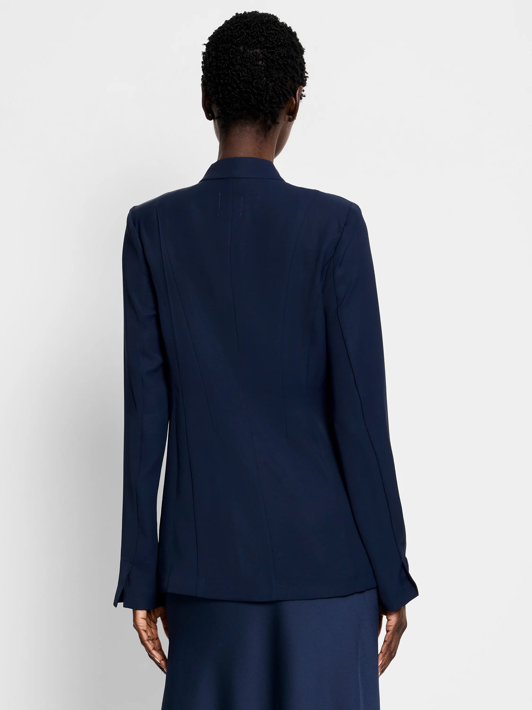 Dark navy blazer, long sleeves, back view.  Seamed detail at back.  Model wears matching skirt.